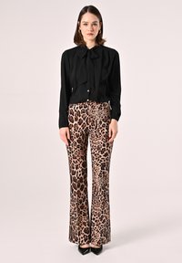 Blusa nera con dettaglio a fiocco, abbinata a pantaloni a zampa d'elefante con stampa leopardata beige. Tacchi neri lucidi completano l'outfit.