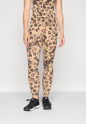 Leopardmønstret leggings i beige med sorte og brune pletter, lavet af strækbart materiale; parret med sorte træningssko.
