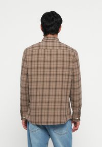 Brun och beige rutig skjorta med långa ärmar, knappmanschetter och rak nederkant; tillverkad av textil med struktur och en yoke-seam på baksidan.