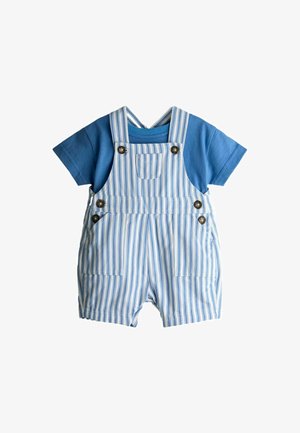 Chemise bleue à manches courtes associée à une salopette courte rayée verticale blanche et bleue avec fermetures à boutons et poches avant.