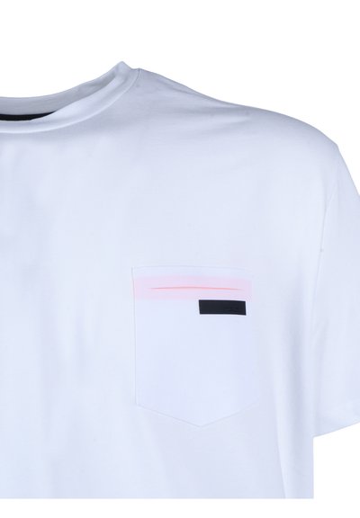 Tricou alb cu guler rotund și buzunar la piept, cu o dungă roz pal și o etichetă mică neagră dreptunghiulară.