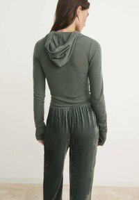 Zelena dukserica dugih rukava s kapuljačom, u kombinaciji s tamnozelenim baršunastim hlačama s elastičnim pojasom. Prilagođenog kroja s mekanom teksturom.