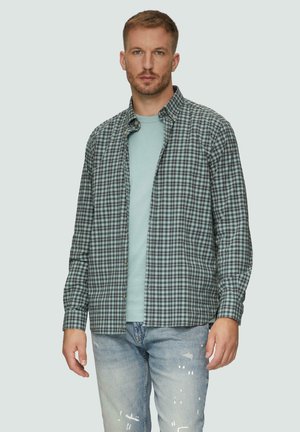 Heren overhemd met knoop in een groen en marineblauw ruitpatroon, vervaardigd uit lichtgewicht stof; gecombineerd met een lichtblauw T-shirt eronder en versleten jeans.