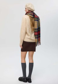 Maglione di lana crema, gonna a maglia marrone, calze al ginocchio grigie, scarpe nere. Sciarpa a quadri con accenti rossi, blu e verdi. Accessorio berretto.