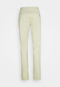 Pantalon beige clair à jambes droites vu de dos avec deux poches passepoilées et un petit logo sur la poche droite.