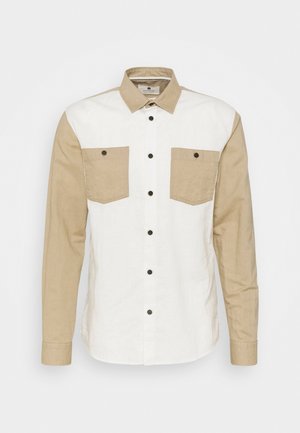 Camicia con bottoni caratterizzata da un corpo bianco e maniche beige, con due tasche frontali, bottoni scuri e un design con colletto classico.
