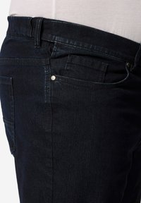 Vaqueros de mezclilla azul oscuro que presentan un diseño clásico de cinco bolsillos, trabillas para el cinturón y un ligero brillo en una textura suave.