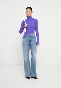 Maglione viola a collo alto con righe, maniche lunghe, abbinato a jeans larghi chiari strappati e décolleté nere a punta. Borsa rosa.
