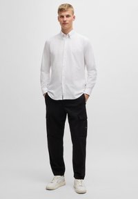 Witte lange mouwen button-up shirt met een kraag, gecombineerd met losse zwarte cargobroek en witte sneakers. Eenvoudig, strak ontwerp.