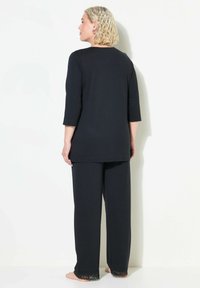 Schwarzes Loungewear-Set mit einem Top mit dreiviertelärmel und lockeren Hosen. Die Hosen haben Spitzenakzente am Saum. Glatte Textur.