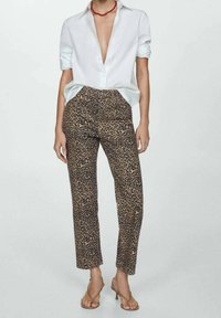 Pantalon imprimé léopard en tissu marron et noir, à coupe slim et longueur cheville, associé à une chemise blanche à col.