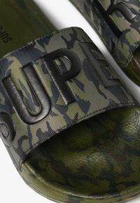 Groene camouflageslippers hebben een brede, gestructureerde zwarte band met "SUPER" in reliëf. De voetbed is glad en gevormd voor comfort.