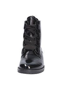 Bottine en cuir noir brillant avec de grosses lacets noirs passant à travers des œillets métalliques, bout arrondi et semelle en caoutchouc plate.