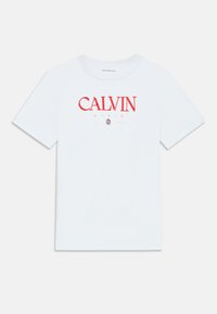 Balta kokvilnas T-kreklu ar īsām piedurknēm, ar sarkanu "CALVIN KLEIN" logotipu priekšpusē. Klasiska apaļa apkakle, bez papildu rakstiem vai akcentiem.