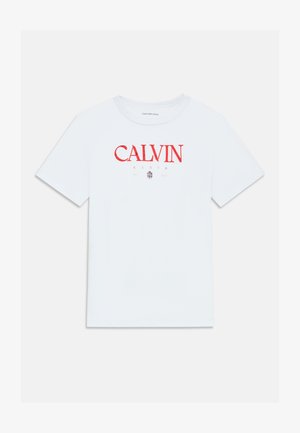 Camiseta de algodón blanca con mangas cortas, que presenta un logotipo rojo de "CALVIN KLEIN" en la parte frontal. Cuello redondo clásico, sin patrones ni acentos adicionales.