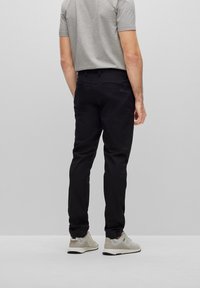 Svarta byxor med slim fit, med en slät textur och subtil logodetalj. Bärs med en grå t-shirt och ljusa sneakers.