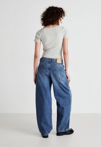Grå kortermet topp kombinert med høy midje, løstsittende blå denimjeans med lærmerke på baksiden og to baklommer.