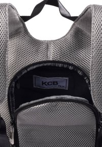 Mochila de malla gris con una superficie texturizada. Presenta un bolsillo frontal con cremallera y un compartimento principal amplio. La marca es visible en el interior.