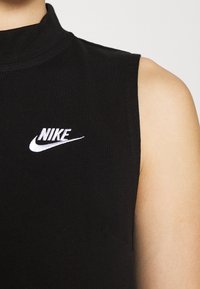 Černý bezrukávový top vyrobený z žebrované tkaniny, který na hrudi zdobí bílé vyšívané logo Nike a má vysoký výstřih.