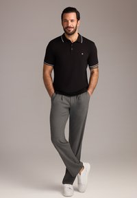 Maglietta polo nera con rifiniture bianche abbinata a pantaloni grigi e sneakers bianche. La maglietta presenta un colletto classico e un dettaglio con logo.