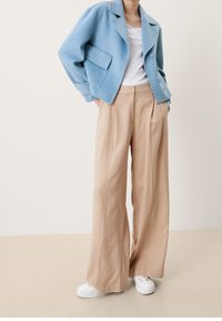 Ljusblå ulljacka med stora fickor, kombinerad med beige vida byxor och vita sneakers. Outfiten visar upp en avslappnad silhuett.