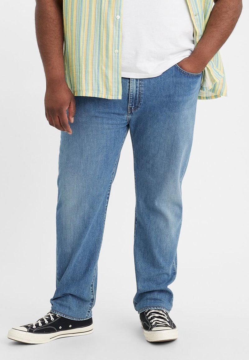 Ljust blå denimjeans med rakt snitt, med en klassisk femfickdesign och subtila blekningar. Matchas med svarta sneakers.