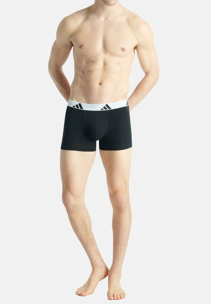 Svarta boxerkalsonger i elastiskt tyg, med ett vitt elastiskt midjeband som har svarta Adidas-logotypdetaljer. Längd till mitten av låret.