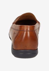 Bruine leren instapschoen met een afgeronde achterkant, voorzien van een zwarte rubberen zool en gestikte details langs de zijkanten.