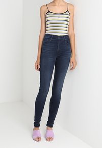 Top de tirantes finos a rayas, jeans ajustados oscuros y sandalias de dedo ligeras de color morado claro. Diseño simple con una silueta ceñida.