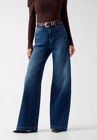 Wijdvallende blauwe jeans van denim met een middelmatige was, met een hoge taille, vijf zakken en een bruin leren riem met een zilveren gesp.