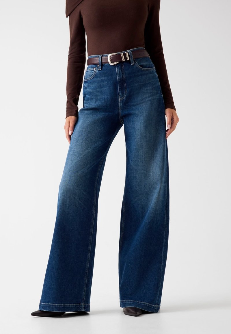 Wijdvallende blauwe jeans van denim met een middelmatige was, met een hoge taille, vijf zakken en een bruin leren riem met een zilveren gesp.