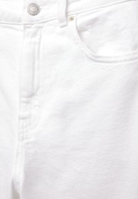 Gros plan sur un jean en denim blanc montrant la ceinture, le bouton argenté, la boucle de ceinture, la poche avant et le détail du rivet.