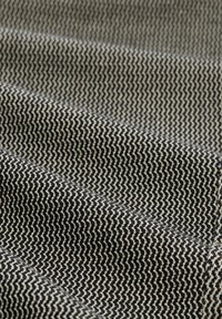 Textiel met een zwart en crème zigzagpatroon. De stof heeft een gladde textuur en is gevouwen, wat diepte en lichtreflecties toont.