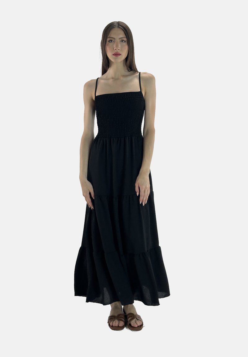 Sort maxi-kjole med spaghetti-stropper, smocket bodice, tiered nederdel og en afslappet pasform. Iført med brune sandaler. Ensfarvet baggrund.