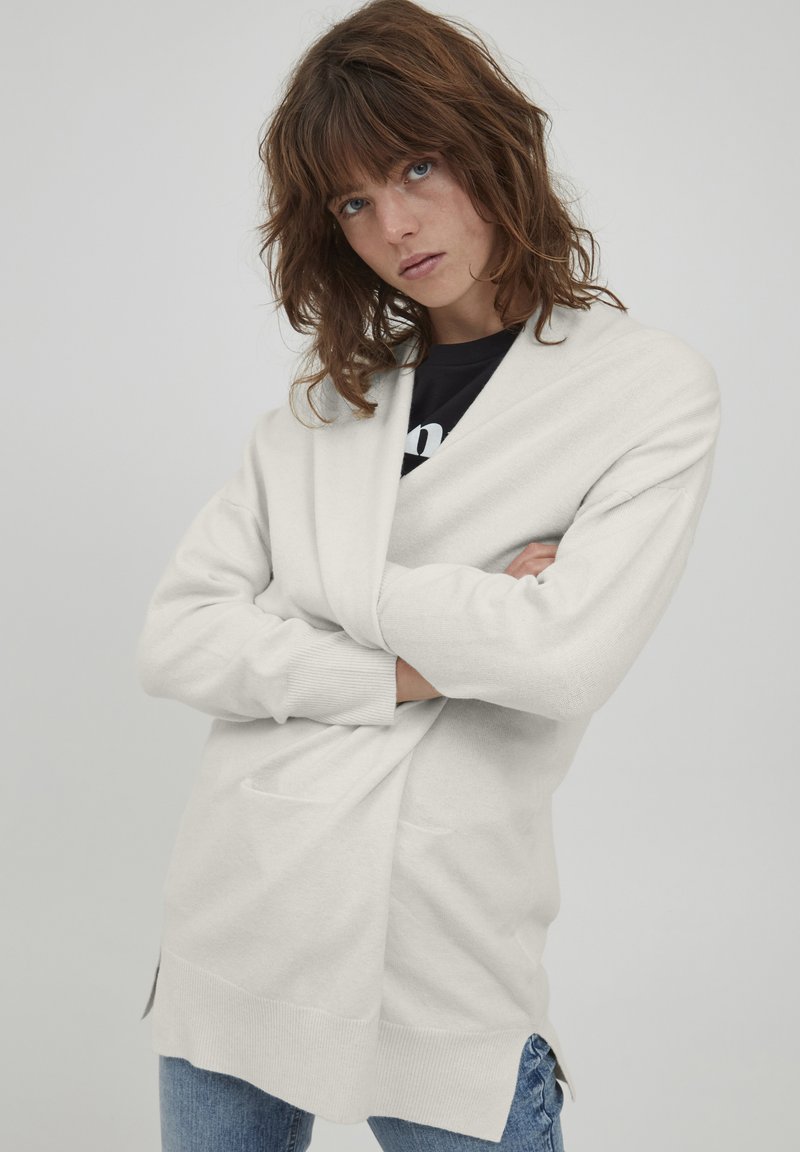 Hellbeige Cardigan mit Wickeldesign, gerippten Bündchen, seitlichen Schlitzen und zwei vorderen Taschen, aus weichem, strukturiertem Stoff.