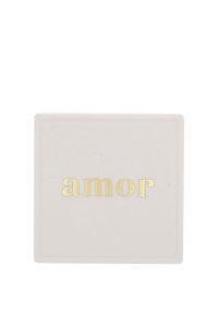 Fyrkantig keramisk underlägg i mjuk rosa, med ordet "amor" i prägling med guldtext. Slät yta, minimalistisk design.