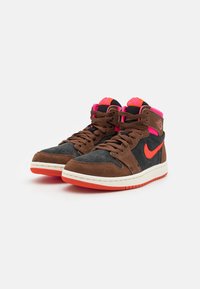 Mid-top sneakers featuring a brown suede upper with black leather accents. Bright pink laces and branding. White midsole with orange outsole.