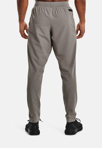 Ljust grå idrottsbyxor med elastisk midja, försedda med två sidofickor och justerbara anklar, i kombination med svarta sneakers.