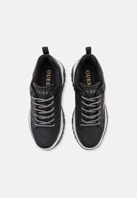 Baskets noires avec un dessus texturé, lacets gris métalliques, semelle extérieure blanche et accents de logo dorés. Comprend une poignée pour un enfilage facile.