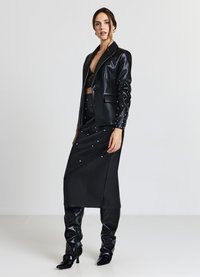 Blazer en similicuir noir à la coupe ajustée, assorti à une longue jupe ornée de rivets argentés et des bottes montantes jusqu'aux genoux.