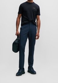 Černé tričko s krátkým rukávem a výstřihem do kruhu s zlatým logem BOSS, spárováno s námořnickými úzkými kalhotami a tmavými teniskami. Doplňky zahrnují černou kabelku přes rameno.