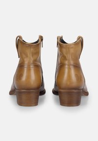 Botas de tobillo de cuero marrón con punta redondeada, tacón bajo y cierre de cremallera. Presentan una textura suave con sutiles detalles de costura.