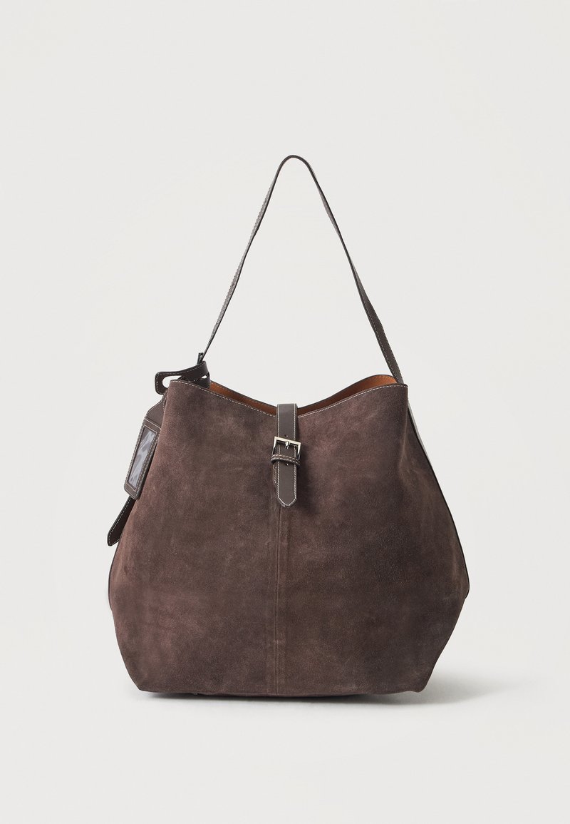 Sac à épaule en daim marron avec une fine bandoulière, fermeture par boucle à l'avant, et une petite étiquette fixée sur le côté.