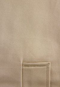 Prim-plan cu material bej cu țesătură diagonală vizibilă și o buzunar dreptunghiular cusut în partea de jos, în centru.