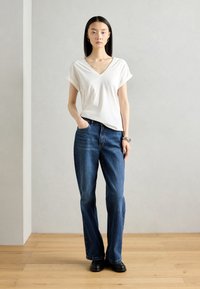 T-shirt blanc à col en V avec des manches roulées, associé à un jean bleu et des chaussures noires. Tissu doux, coupe droite et design classique.