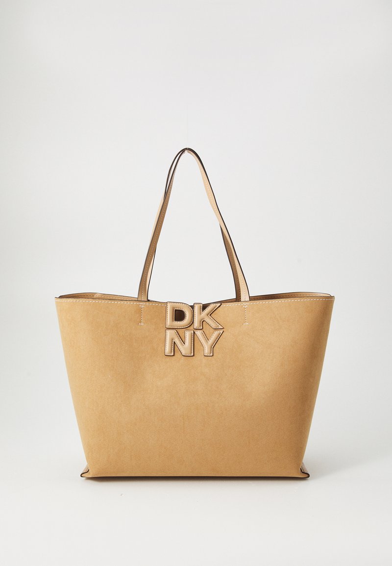 Tan faux suede tote bag with dual handles, featuring a prominent DKNY logo in metallic accents, fine stitching, and an open top design.