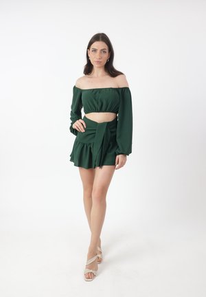 Crop top verde sin hombros con mangas largas y borde volado, combinado con una falda a juego que presenta un lazo en la cintura.