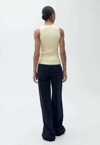 Prúžna, bezrukávová svetložltá blúzka v kombinácii s voľnými tmavými džínsami. Oblečenie má minimálne detaily a voľný strih.