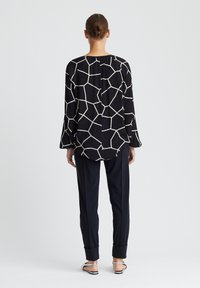 Zwarte lange mouw top met wit geometrisch patroon, gecombineerd met marineblauwe broeken met omgeslagen mouwen; gladde stof, ruime pasvorm en relaxte silhoutte.