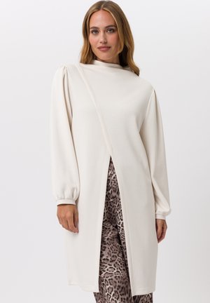 Robe longue crème à manches longues avec un col montant et une fente sur le devant, présentant des manches légèrement bouffantes et une texture lisse. Accentuée par un pantalon à imprimé léopard.